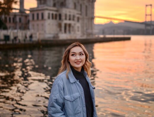 Peaceful solo portrait during sunset in front of Ortaköy Mosque and Bosphorus Bridge — warm golden light reflecting on the water as the tourist smiles softly.