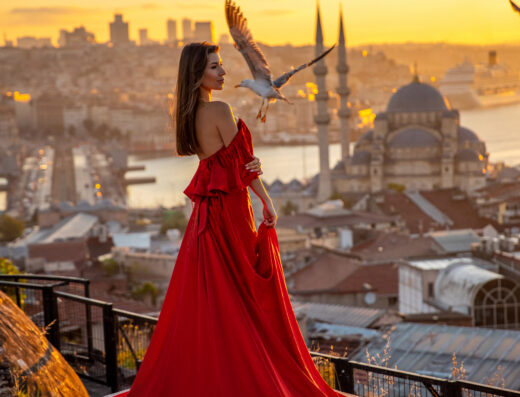 Woman in a flowing red dress watching the sunset over Istanbul with birds flying and a historic mosque in the background